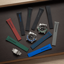 A flat-lay display of various watch strap options and a watch case on a dark brown textured mat. The collection includes multiple silicone watch straps in red, green, blue, black, and gray, along with two stainless steel watch cases, one with a blue bezel insert and one with a green bezel insert.